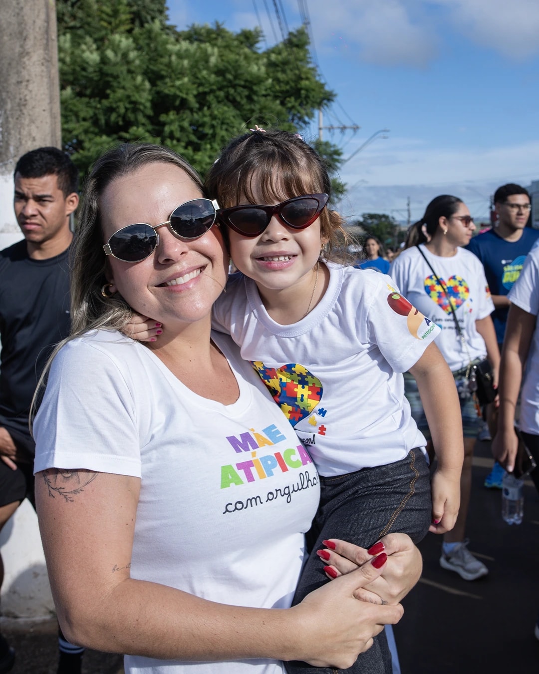 Mãe e filha sorrindo abraçadas durante a Caminhada da Inclusão