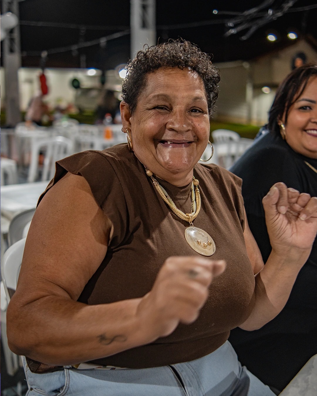 Senhora sorrindo e dançando sentada à mesa na Festa das Famílias