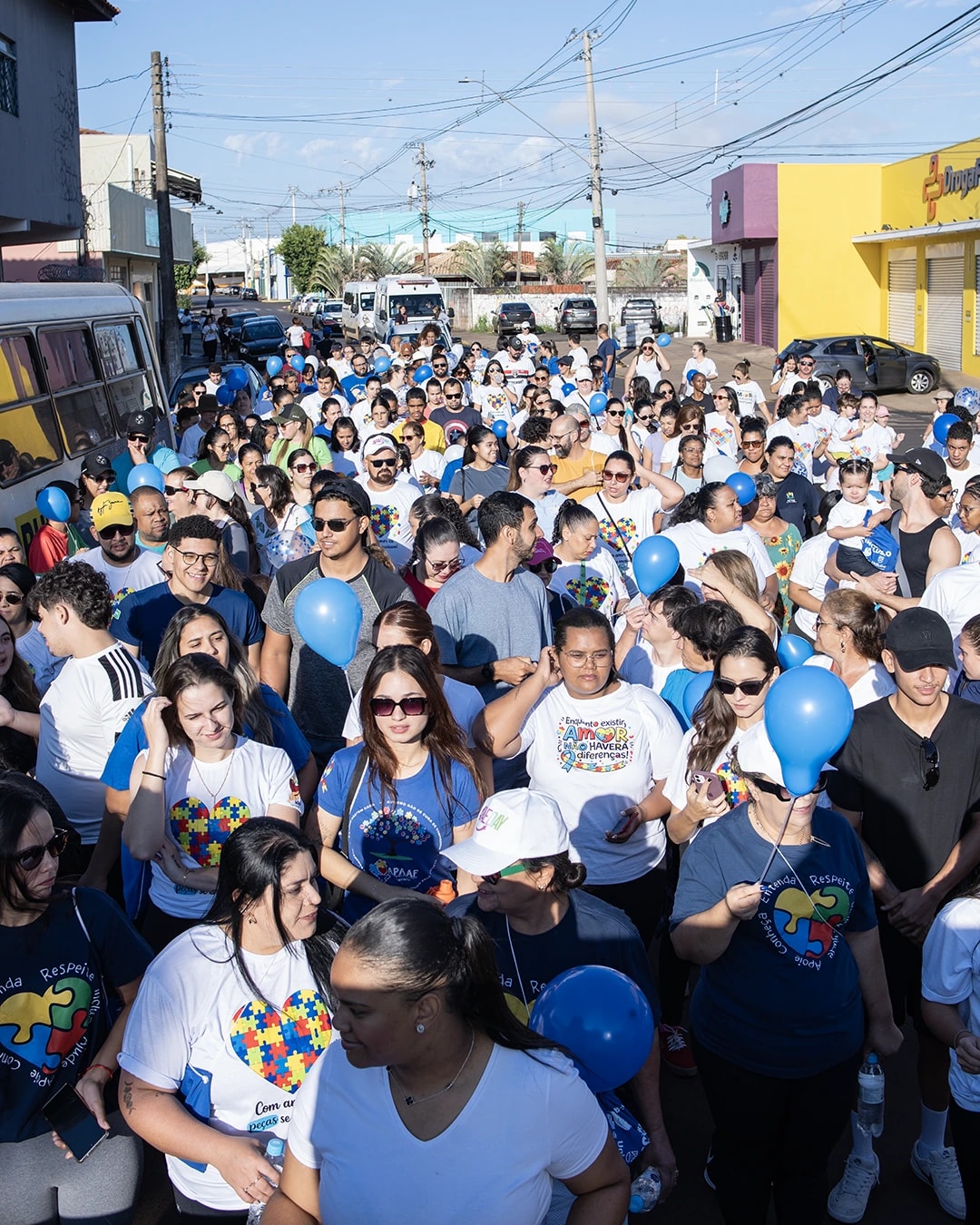 Multidão com camisetas da campanha e balões azuis caminhando pela rua na Caminhada da Inclusão
