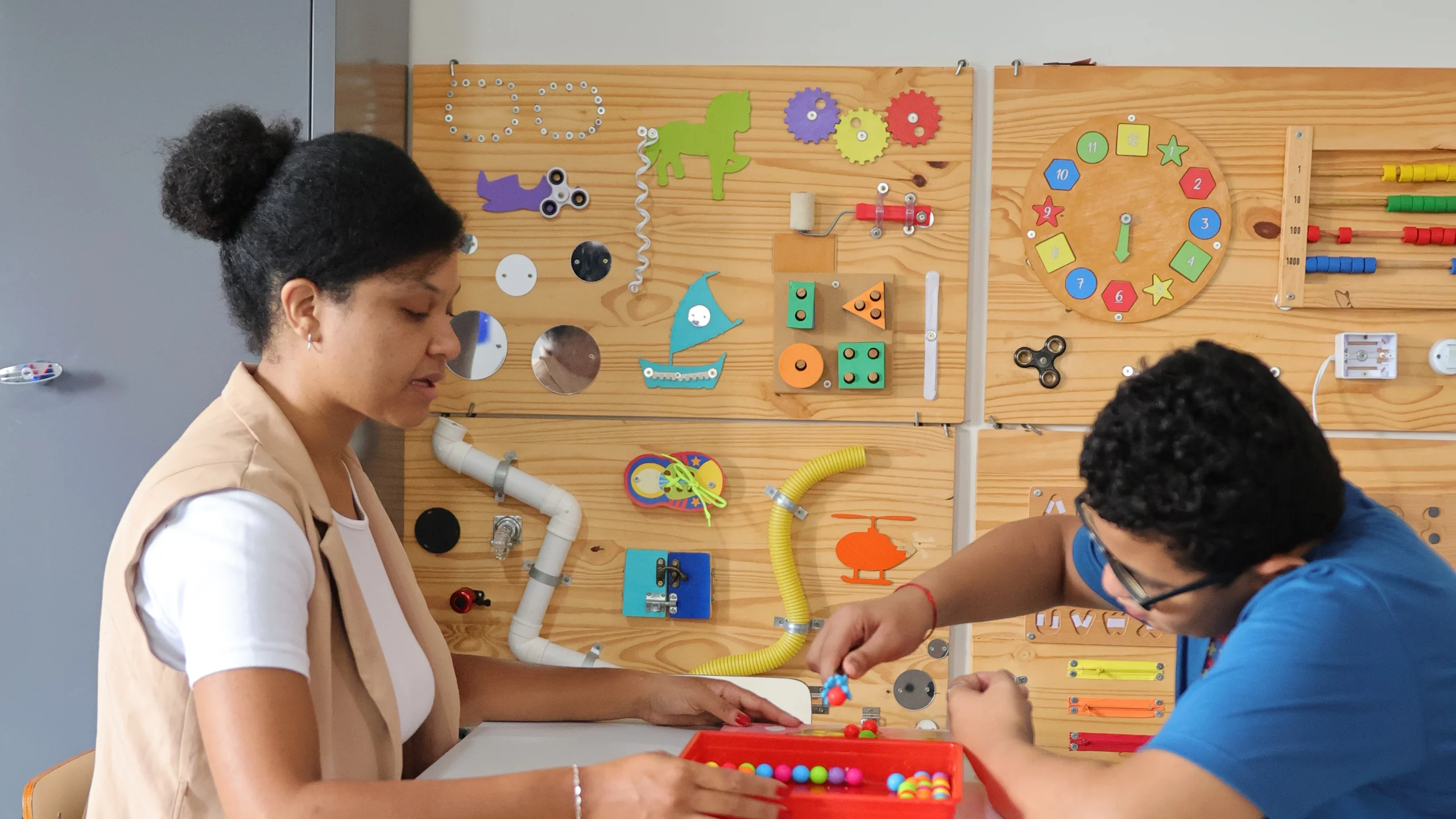 Terapeuta da APAE em atendimento com jovem diante de um painel sensorial