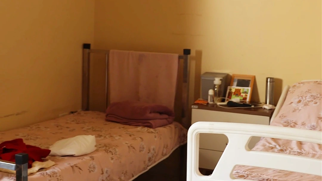 Quarto da Residência Inclusiva, com cama de colcha florida e criado-mudo com porta-retrato